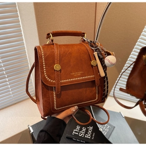 Close-up of brown vintage leather backpack with gold rivets and baseball charm