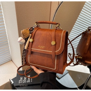 Close-up of vintage brown leather backpack with gold buckles and baseball pendant charm