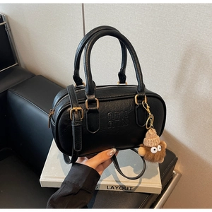 Detail of black Boston bag with textured leather, gold hardware and plush bear charm