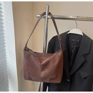 Close-up of brown matte leather shoulder bag featuring adjustable strap and fashion logo patch