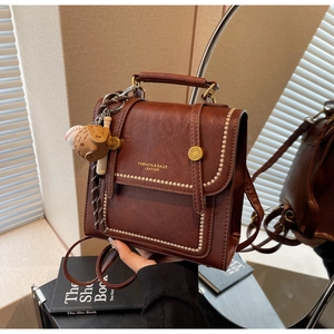 Close-up of vintage brown pebble leather bag with gold rivets and baseball charm