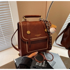 Detail of dark brown vintage faux leather backpack with gold rivets and baseball charm