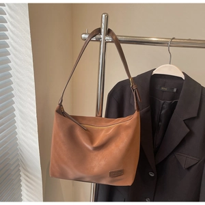 Close-up of brown suede hobo bag with adjustable leather strap and golden logo tag