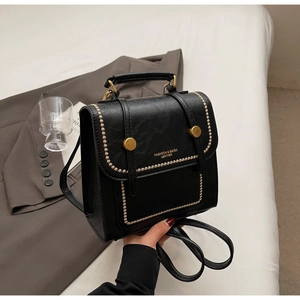 Detail of black faux leather backpack with gold studs and brand lettering on bedding