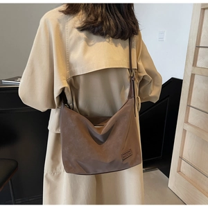 Detail of dark brown suede tote bag featuring a leather logo patch and adjustable strap