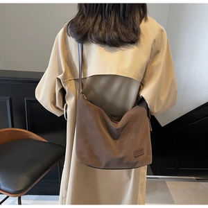 Side view of large dark brown suede hobo bag with adjustable strap on a model