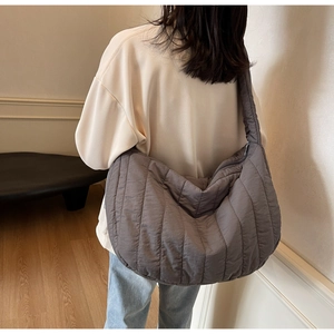 Detailed view of dark grey quilted crescent tote bag with vertical stripes shown on a model