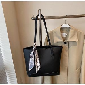 Detail of black pebbled leather tote bag with decorative floral silk scarf on a trench coat