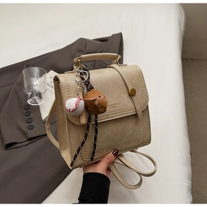 Detail showing beige retro backpack with gold clasp, baseball charm, and leather texture