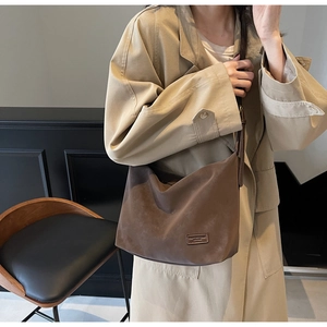 Brown faux suede hobo bag on shoulder featuring a rectangular fashion leather patch detail