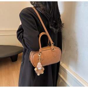 Detail of a brown leather barrel bag featuring embossed logo and cute plush charm