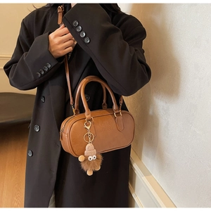 Detail of a brown leather cylinder bag with brand embossing and a cute plush toy charm