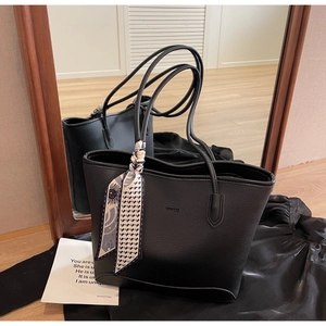 Detail of black pebbled leather tote bag with logo and floral silk scarf on the handle
