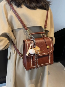 Vintage reddish brown leather backpack with baseball charm and contrast stitching