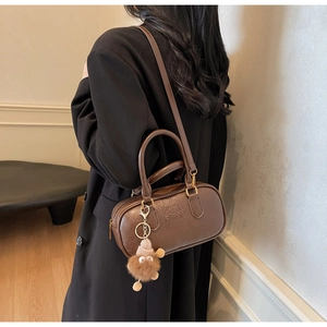 Brown leather cylinder handbag worn by a model in a black coat for a stylish look