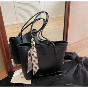Detail of black pebbled leather tote bag with floral silk scarf and embossed logo