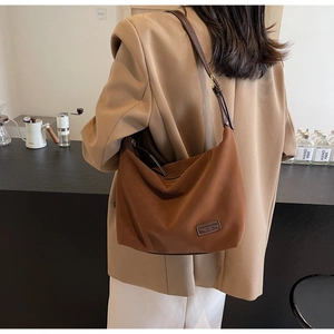 Detail view of brown faux suede hobo bag worn with a khaki blazer in a studio setting