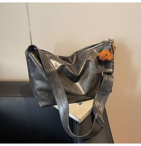 Détail d'un sac cabas noir texturé avec bandoulière large et charm d'ours en peluche