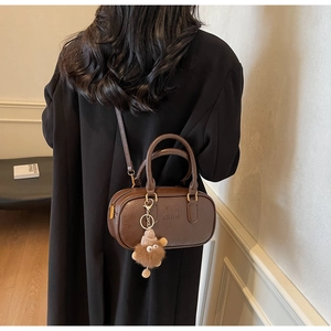 Brown vintage faux leather pillow bag with plush charm shown worn by a model in a suit