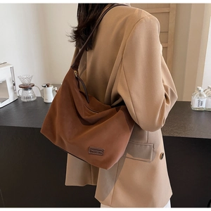 Detail of the brown suede hobo bag featuring a stitched leather logo label on the front