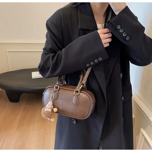 Detail view of dark brown retro Boston bag with embossed logo and plush toy charm