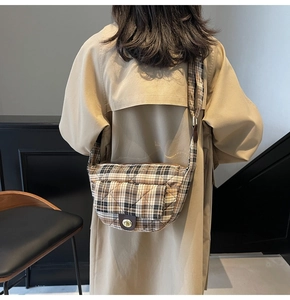 Detail view of the quilted plaid crossbody bag with a golden twist lock on a beige coat