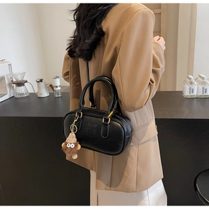 Chic black Boston bag with embossed text and plush charm styled on a model in a cafe
