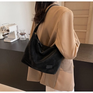 Detail of a black matte hobo bag worn with a khaki blazer in a modern cafe setting