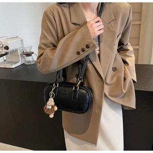 Detail of black leather cylinder bag with embossed logo and brown plush charm