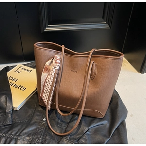 Close-up of brown litchi grain leather tote bag with printed silk scarf on a black jacket