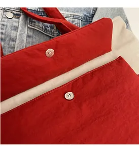 Detail of red nylon tote bag featuring silver magnetic snap closure and neat stitching