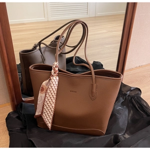Detail of brown litchi grain leather tote bag featuring a decorative silk scarf and logo