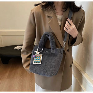 Detail of grey plush bucket bag with fuzzy texture, shoulder strap and calculator charm