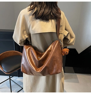 Détail d'un grand sac hobo marron rétro avec large bandoulière et pendentif ours en peluche