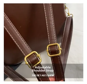 Close-up of adjustable brown leather shoulder strap with gold buckle and white stitching