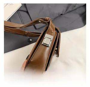 Close-up of silver rectangular buckle and smooth dark brown leather on square shoulder bag