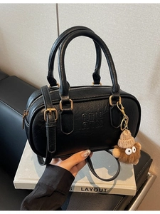 Retro black leather Boston bag with gold hardware and plush charm on white books
