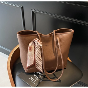 Detail of brown lychee leather tote bag with WWAU logo and silk scarf on handle