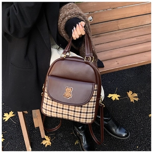 Detail of dark brown checkered backpack with bear patch held against autumn park background