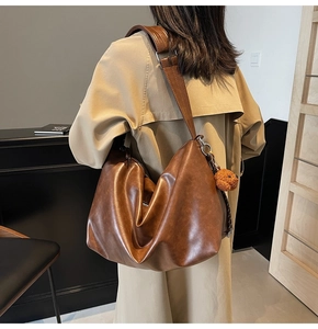 Détail d'un sac cabas en cuir marron mat avec bandoulière large et pendentif d'ours