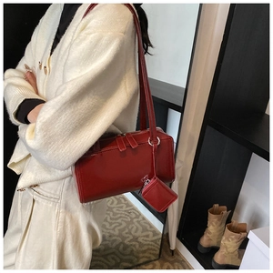 Close-up of red glossy leather shoulder bag with matching mini pendant and dual zippers