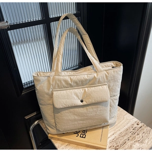 Detailed close-up of quilted beige tote bag with functional front flap pocket and snap