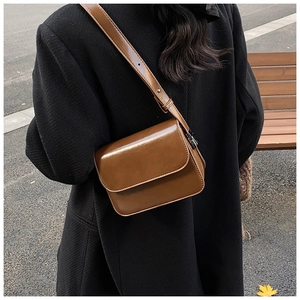 Outdoor look of brown leather square crossbody bag worn over a classic black coat