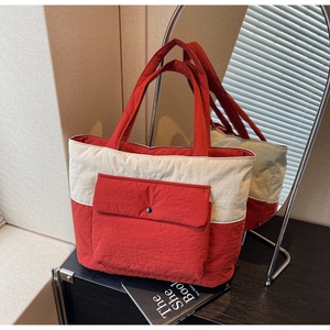 Detail of quilted canvas tote bag with contrast red handles and front flap pocket