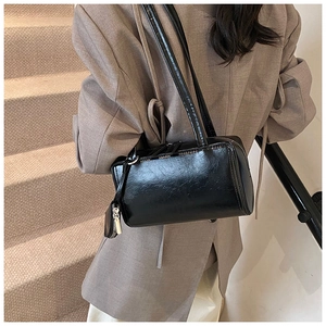 Model wearing a black glossy leather shoulder bag with silver zipper in a modern setting
