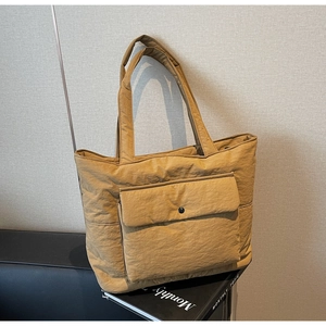 Detail view of khaki nylon tote bag featuring a metal snap front pocket on a book