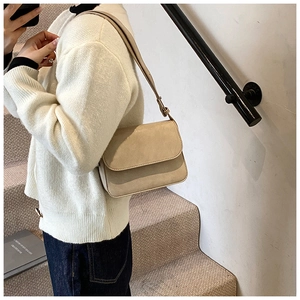 Close-up of minimalist beige crossbody bag with adjustable strap worn on the shoulder