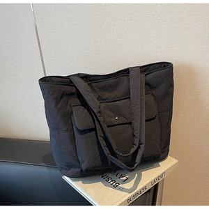 Close-up of a black quilted tote bag featuring a large front flap pocket and metal buckle