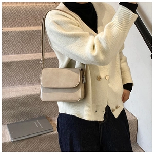 Close-up of minimalist beige rectangular crossbody bag worn by model on stairs