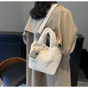 Detail view of plush beige bucket bag with colorful calculator charm and knit strap